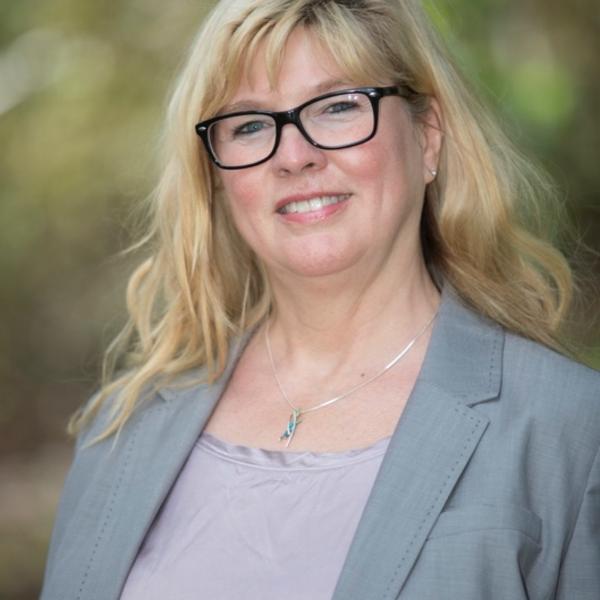 A smiling female faculty member with shoulder length blond hair wearing a grey suit jacket