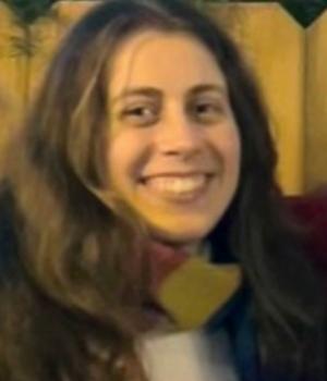 Smiling brown-haired woman wearing a scarf and white sweater