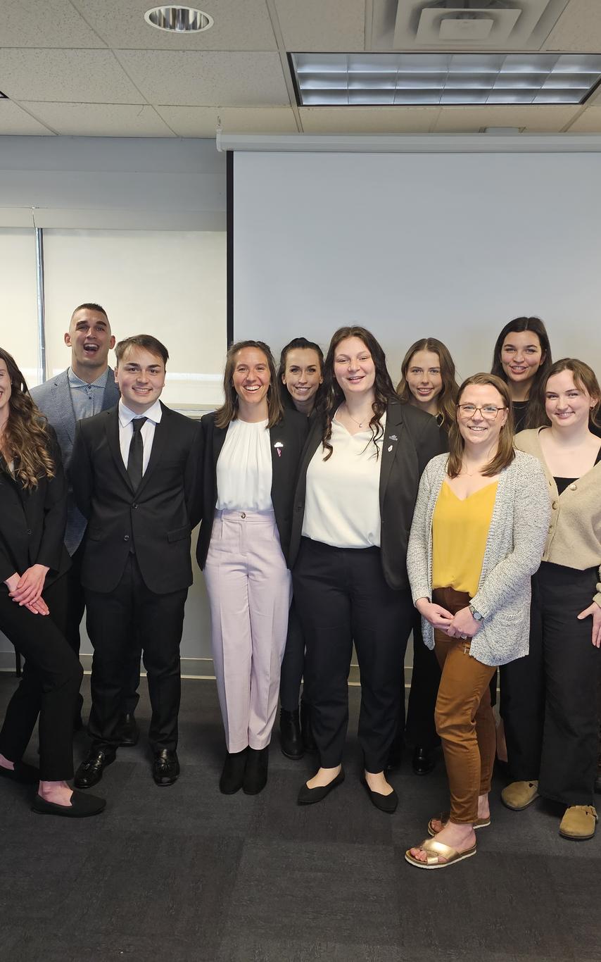 a group of fifteen students and faculty professionally dressed nd smiling standing in a line